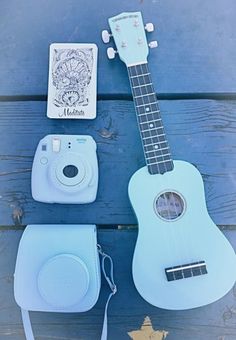 a blue ukulele sitting on top of a wooden table next to a camera