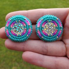 a pair of colorful beaded earrings on someone's hand in front of a green field