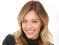 a woman with blonde hair smiling at the camera, wearing a black top and lace sleeves