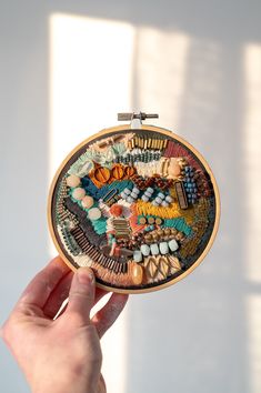 a hand holding a small embroidery kit with beads and other items in it, on a white background