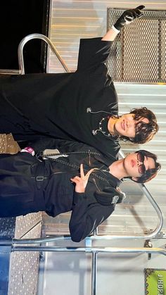 two young men standing next to each other in front of a metal rail with luggage