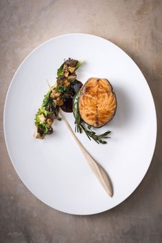 a white plate topped with a pastry and salad next to a wooden utensil