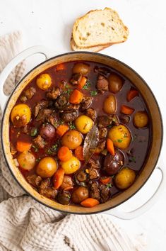 a pot filled with stew next to bread on top of a white cloth and napkin