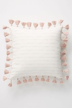 a white pillow with pink tassels on the front and back of it, against a white background