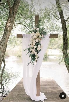 a cross decorated with white flowers and greenery on a wooden platform next to water