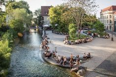 many people are sitting on benches by the river and some trees in front of them