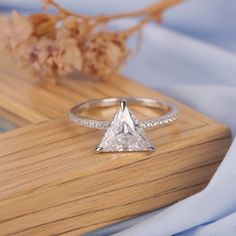 a white diamond ring sitting on top of a wooden table next to a dried plant