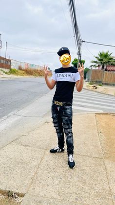 a man with a smiley face painted on his shirt and jeans is standing in the street