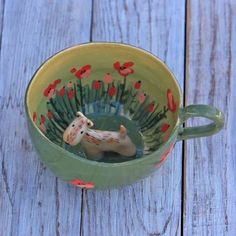 a ceramic horse in a green cup with red flowers on the outside and inside, sitting on a wooden table