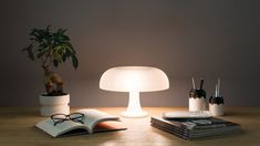 a table with a lamp, book and glasses on it next to a potted plant