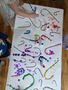 a child is painting letters on a large sheet of white paper with colored beads and crayons