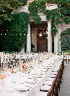 an outdoor wedding reception with long tables and white linens, greenery and hanging lights