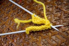 two knitting needles are hooked up to the ends of a yellow piece of yarn that has been crocheted