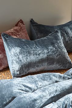 three velvet pillows sitting on top of a bed