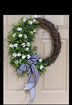 a wreath with white flowers and green leaves hangs on the front door, next to a striped ribbon