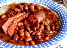 a bowl filled with beans and meat on top of a blue checkered table cloth