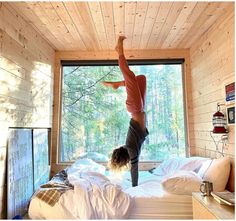 a person doing a handstand on a bed in front of a large window