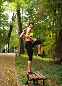 a young woman is doing exercises on a bench in the park while listening to music