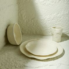 three white plates and two cups sitting on a counter next to each other in a room