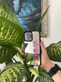 a woman holding up her phone case in front of a plant with the words awme on it