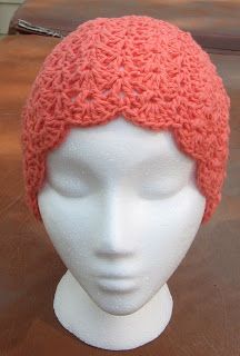 a white mannequin head wearing an orange crochet hat on top of a wooden table