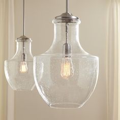 two clear glass pendant lights hanging from a ceiling fixture in a living room or kitchen