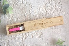 a pink toothbrush in a wooden box on a white surface with leaves and flowers