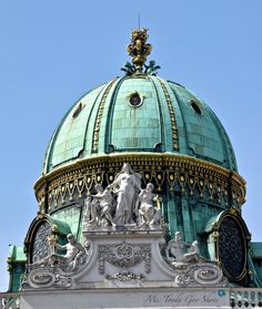 the top of a building with statues on it's sides and a blue dome in the background