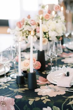 the table is set with white and pink flowers, black candle holders, and silverware