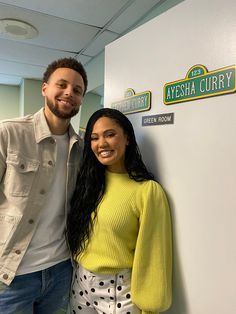 a man standing next to a woman in front of a sign that says ayesha curry