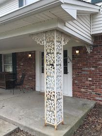 a porch with a white pergolan on the side of it and brick building in the background