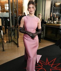 a woman in a pink dress and black gloves standing on a red carpet with other people