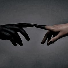 two hands reaching out towards each other with black paint on their fingertipss, against a gray background