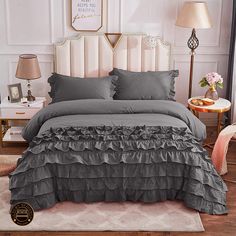 a bed with grey ruffled bedspread and two lamps on the side tables