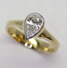 a yellow and white gold engagement ring with a pear shaped diamond in the center, on a plain surface