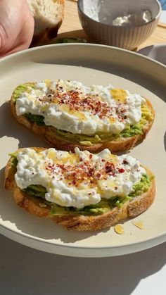 two pieces of bread with cream cheese and avocado on them sitting on a plate