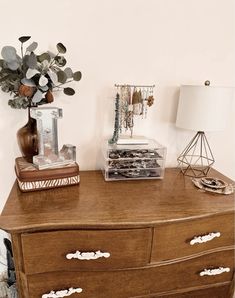 a wooden dresser topped with lots of drawers next to a lamp and vase filled with flowers