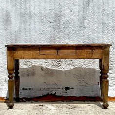 an old wooden table sitting in front of a white wall