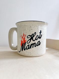 a white mug with the words hot mama on it sitting on a table next to a wall