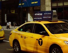 a yellow taxi cab driving down a street next to tall buildings