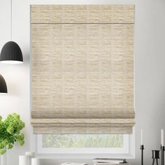 a white kitchen with a window covered in roman blind shades and black pendant lights hanging from the ceiling