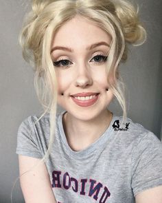 a woman with blonde hair wearing a grey t - shirt and smiling at the camera