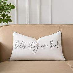 a pillow that says, let's stay in bed on a couch next to a potted plant