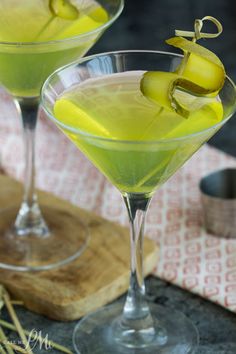 two glasses filled with yellow liquid on top of a wooden cutting board