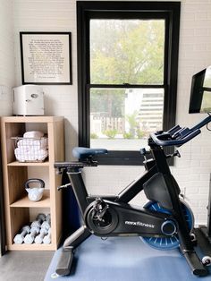 an exercise bike in front of a window and shelves with items on it for storage