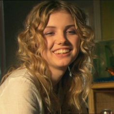 a woman with long curly hair smiling at the camera while sitting in front of a cabinet