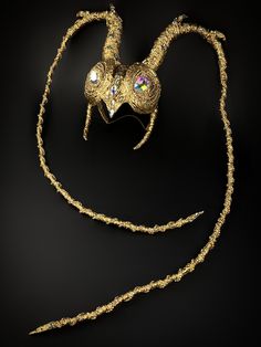 a gold mask on a black background with a long chain attached to the headpiece