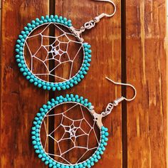 two pairs of earrings with turquoise beads and silver hooks on a wooden surface, one has a spider web in the center