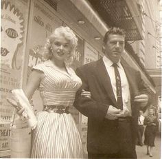 a man and woman standing next to each other in front of storefronts with advertisements on the wall