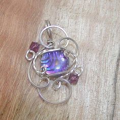 "A glowing, gorgeous hot purple 10mm round paua shell cabochon from New Zealand, with swirls of black and hints of lavender and pink. Set in delicate swirls of sterling silver wire. With two 4mm amethyst-purple Swarovski crystal beads for a bit of glitter. It makes a great gift or stocking stuffer--it's affordable, and who doesn't love purple! This little darling is the perfect size in a sure-to-get-noticed color for wearing every day! It measures about 1-1/4\" long by 3/4\" wide, with a round b Purple Wire Wrapped Jewelry For Party, Party Wire Wrapped Purple Jewelry, Party Purple Wire Wrapped Jewelry, Unique Swirl Jewelry As A Gift, Wire Wrapped Swirl Jewelry As Gift, Unique Purple Round Pendant Jewelry, Purple Wire Wrapped Round Jewelry, Purple Cabochon Round Pendant Jewelry, Handmade Purple Spiral Jewelry